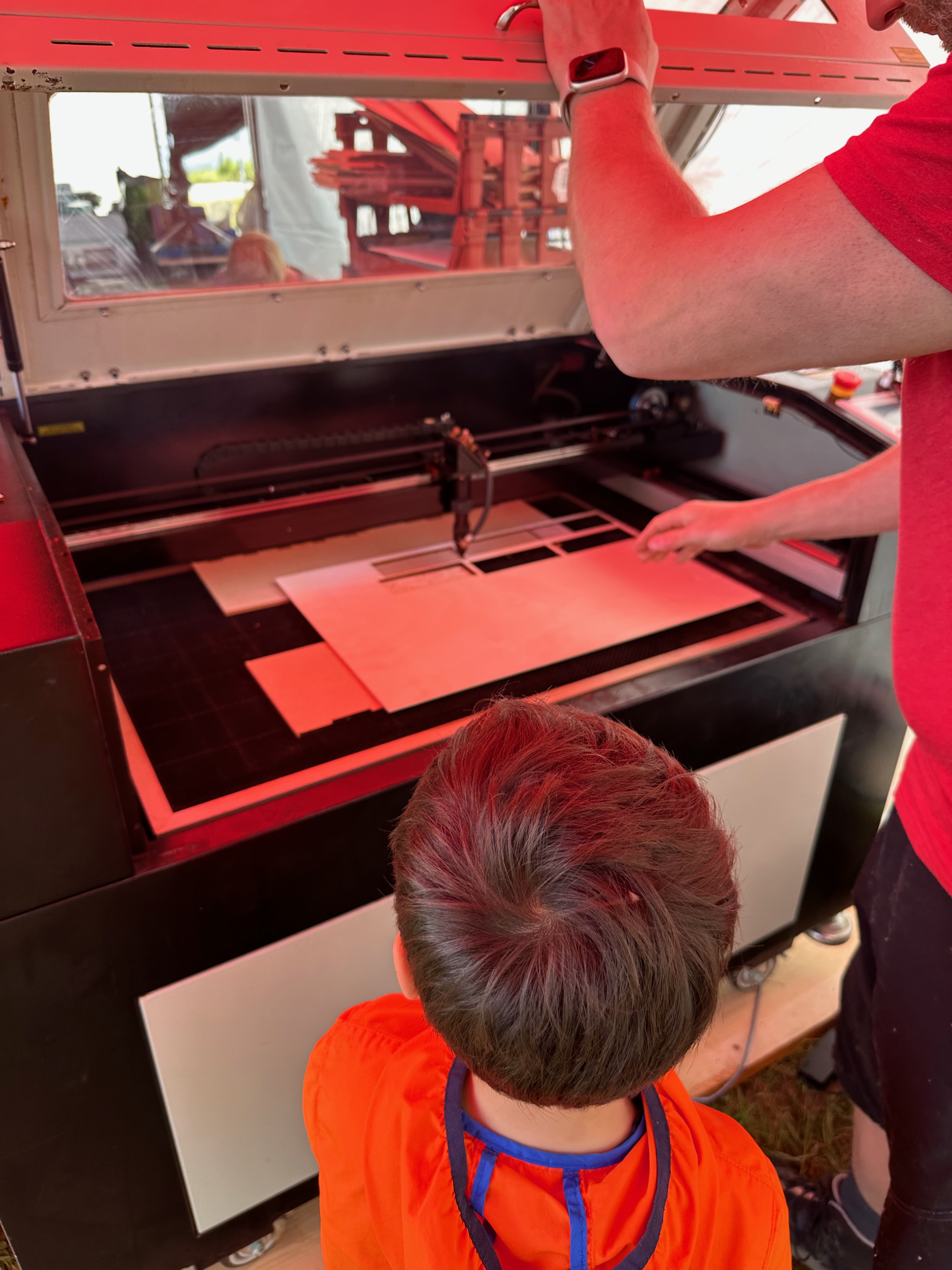 A boy stands looking at a sheet of wood being loaded into a laser cutter.
