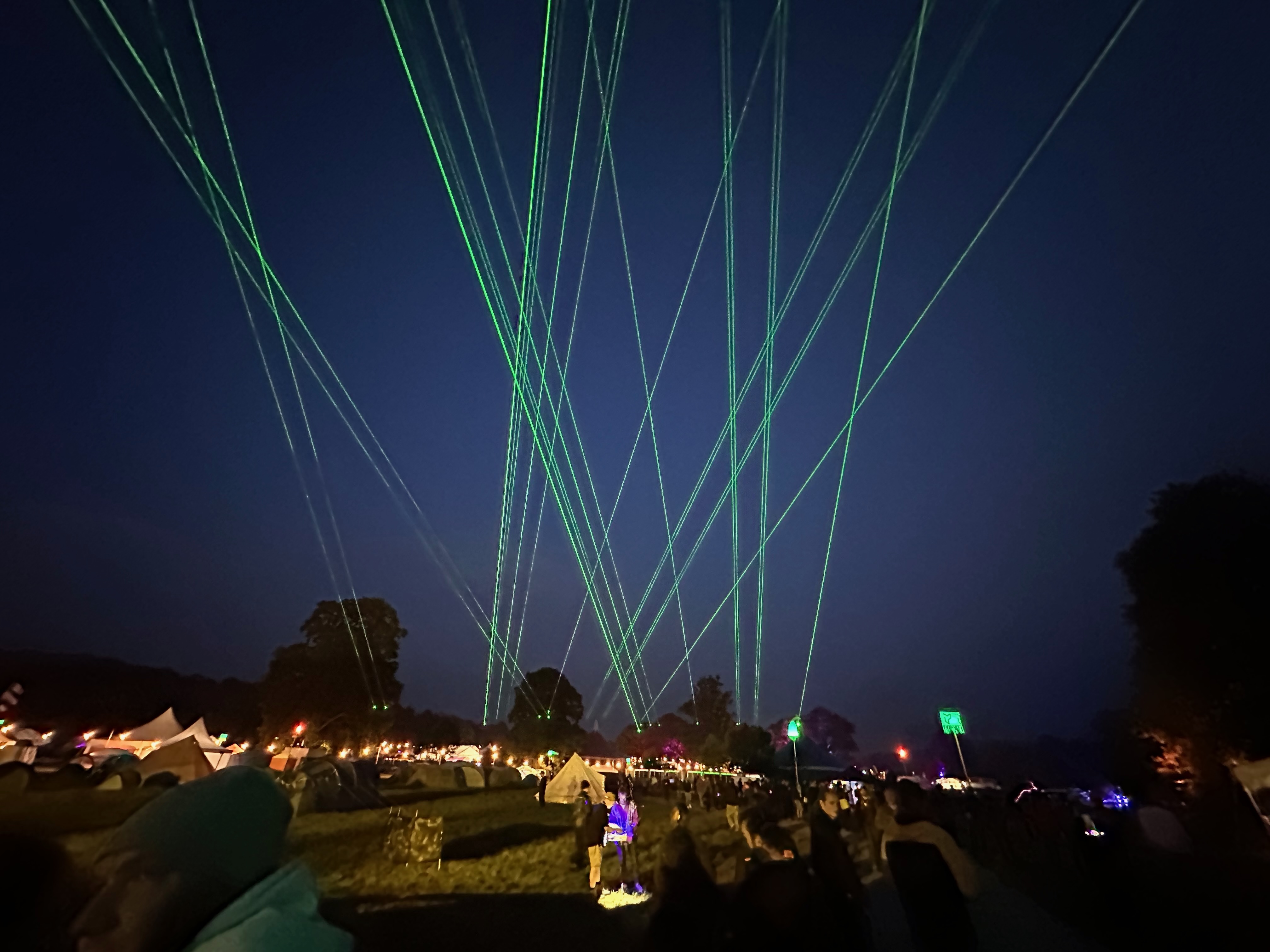Green lasers light up the night sky above a campsite.