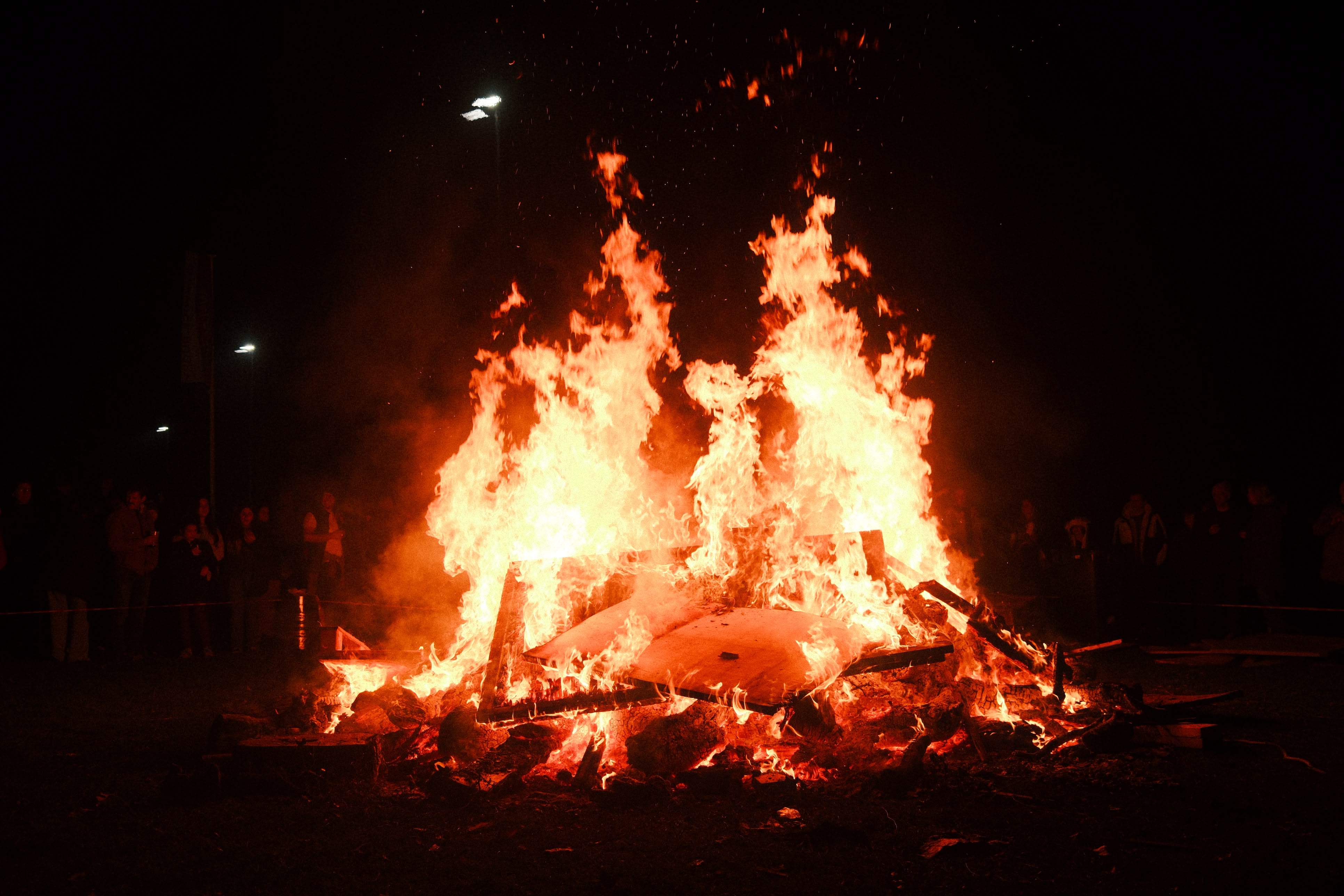 a photo of a bonfire at night, the faces of people on the far side of the fire lit by the glow from the fire