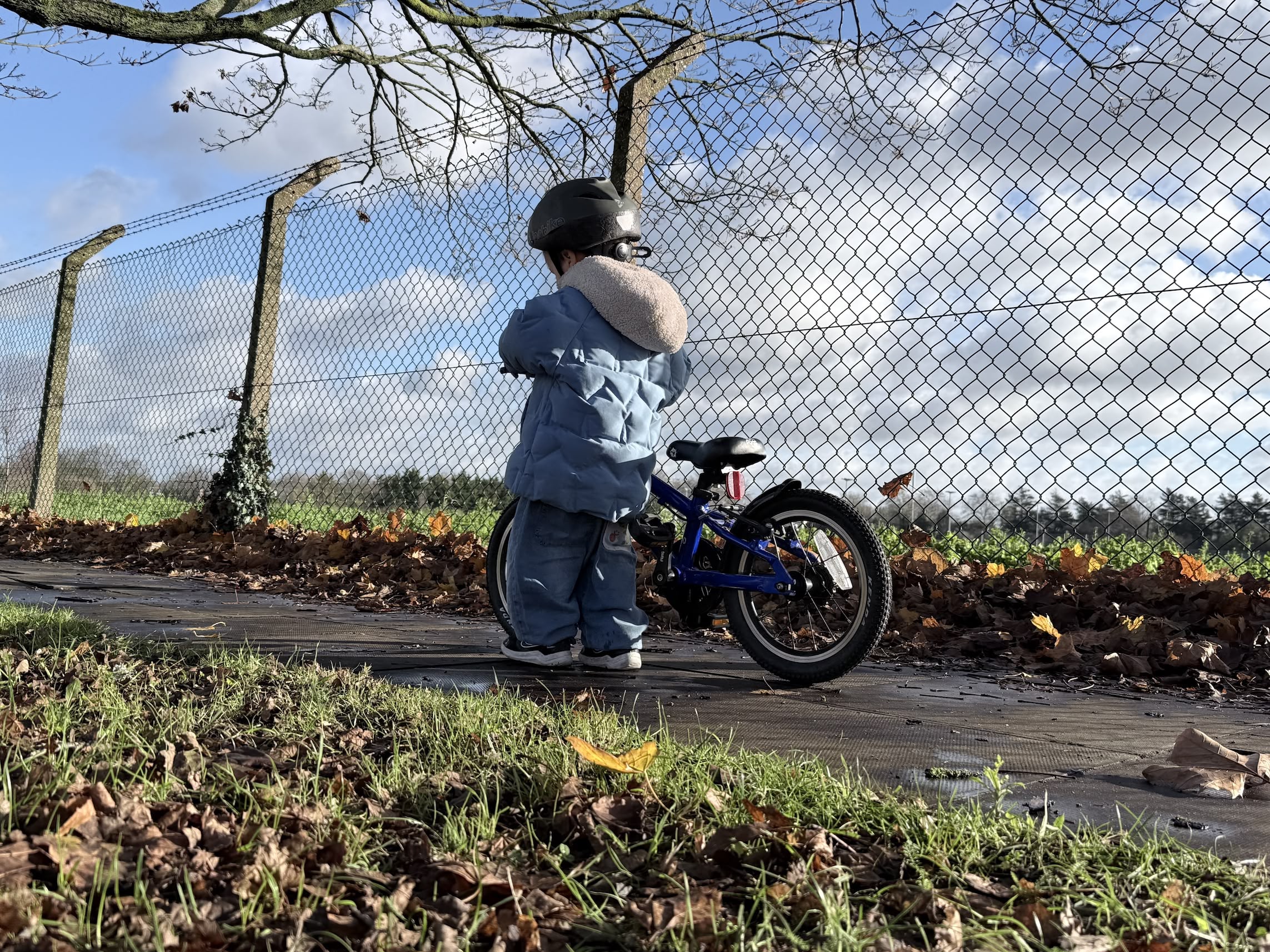 A young boy standing next to his small bike looking away from the camera