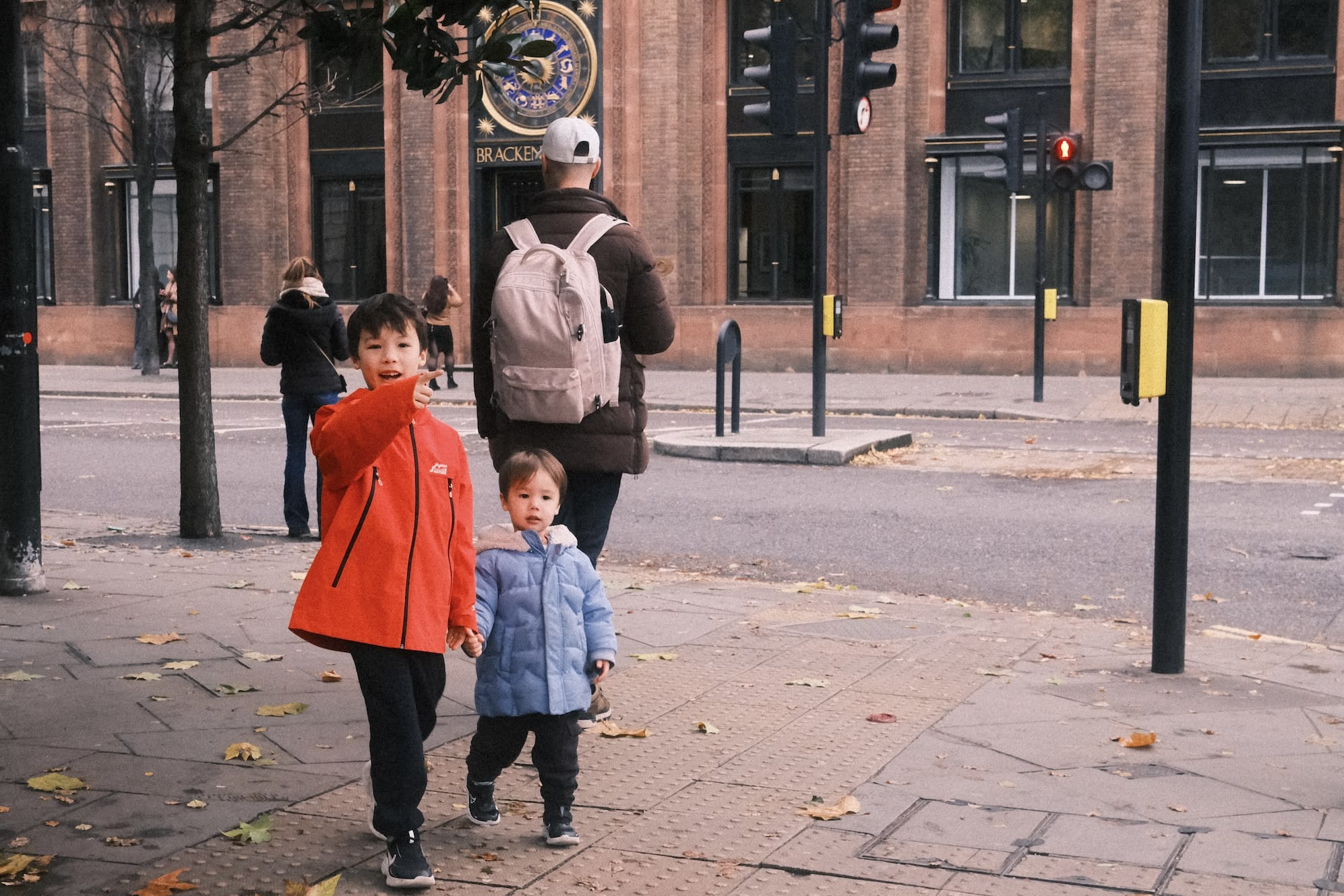 Two boys walk on the streets of London, the older points to something behind the camera