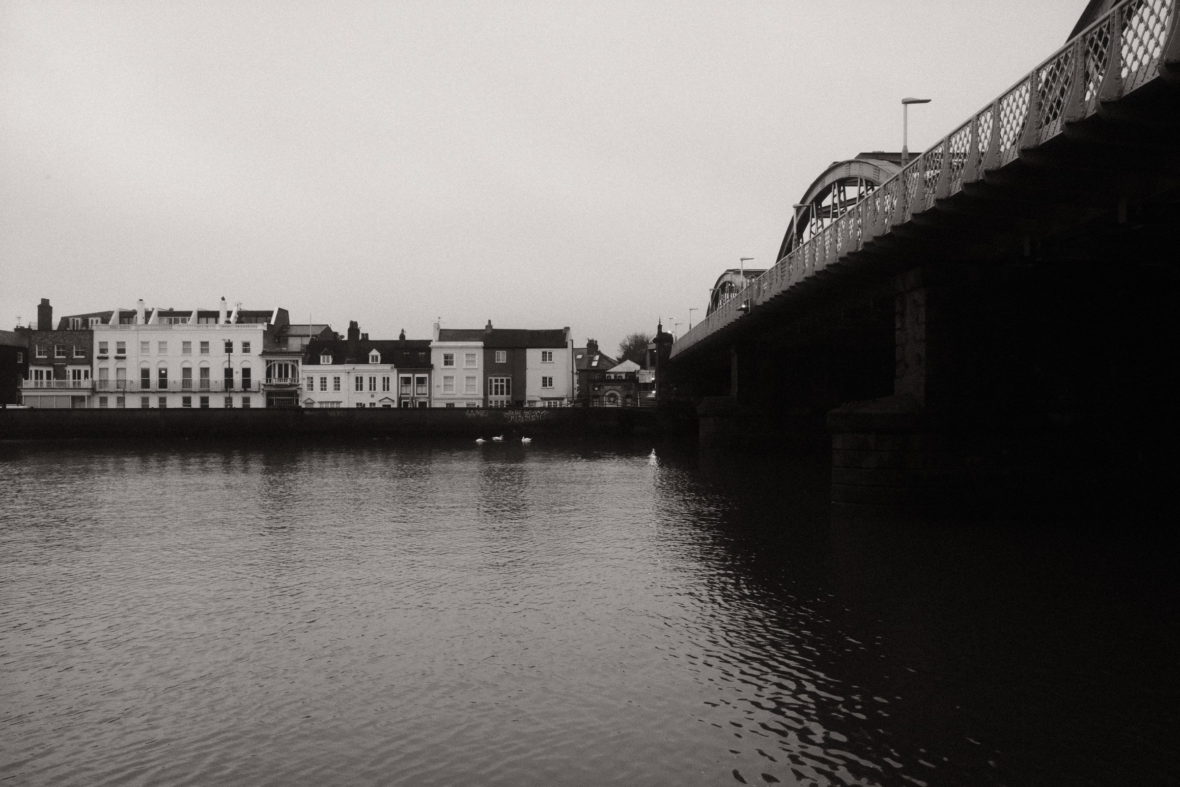 a black and white photo looking over the River Thames towards Barnes Bridge station