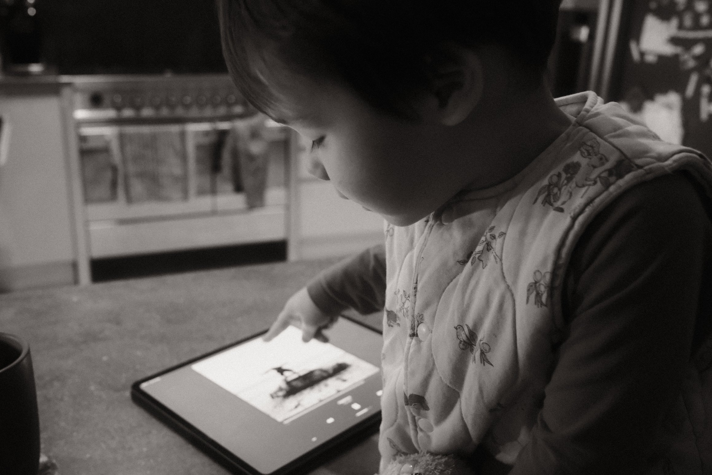 A black and white photo of a young child pointing at an iPad. On the iPad is the cover of 1975's Being Funny in a Foreign Language.