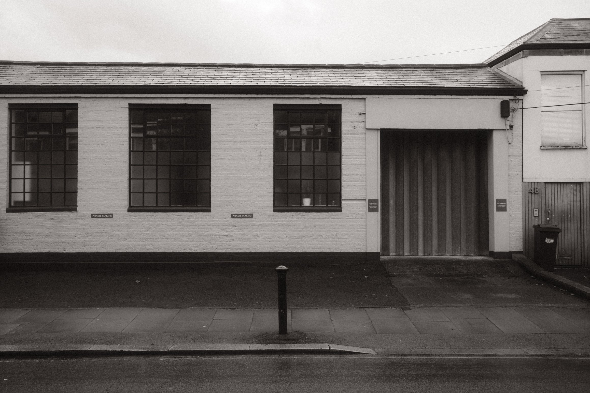 Black and white photo of a small warehouse style building. The doors are closed.