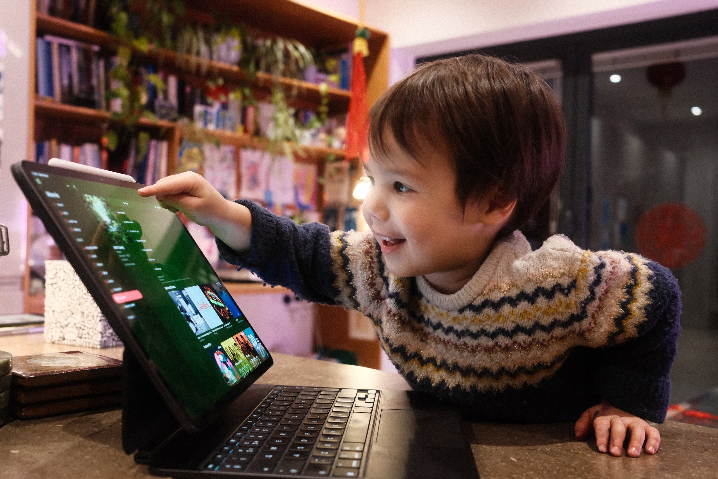 Smiling, a small boy points at an album cover on an iPad.