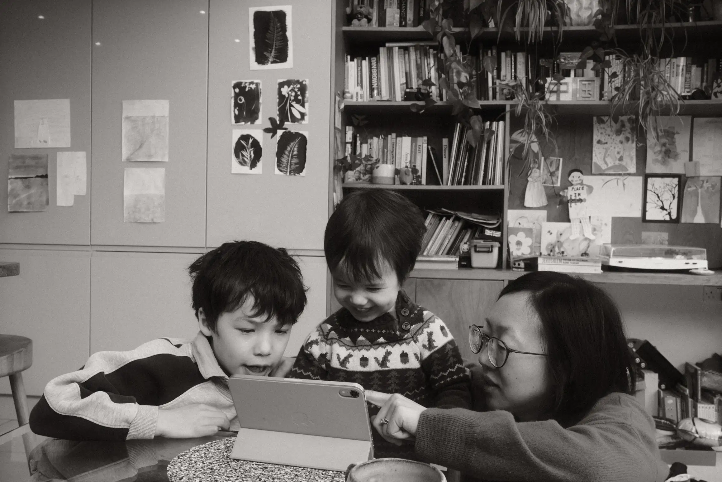 Two boys and their mother huddle around an iPad. The youngest is in the middle smiling. The mother points to something on screen.