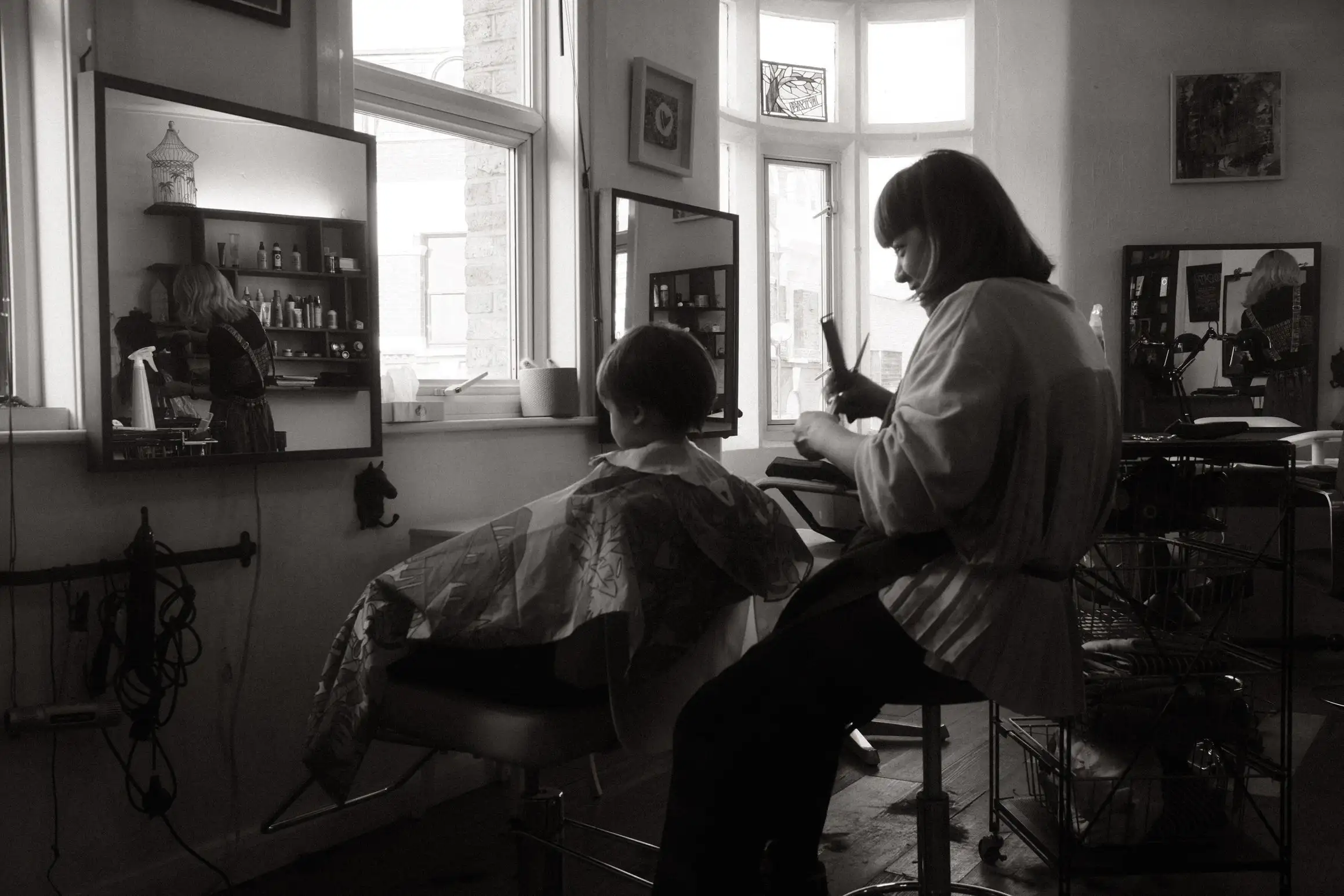 A black and white photo of a young boy sat having his haircut