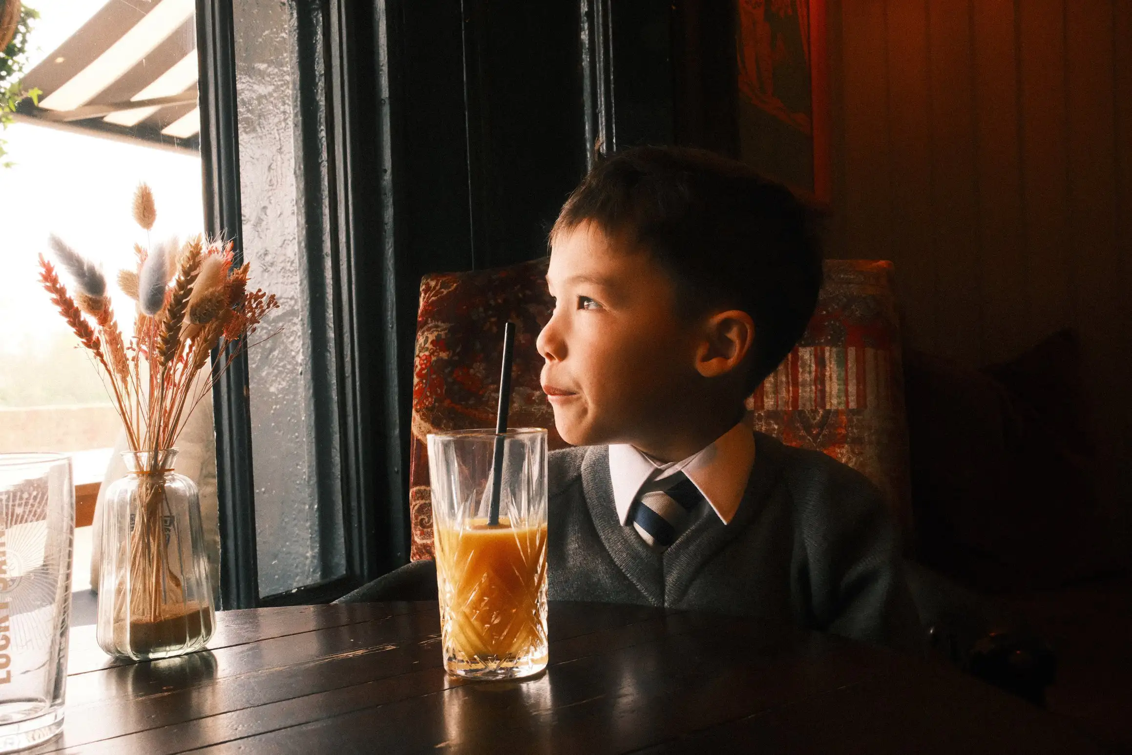 a boy looks stares out of the pub window, half a glass of orange juice on the table in front of him