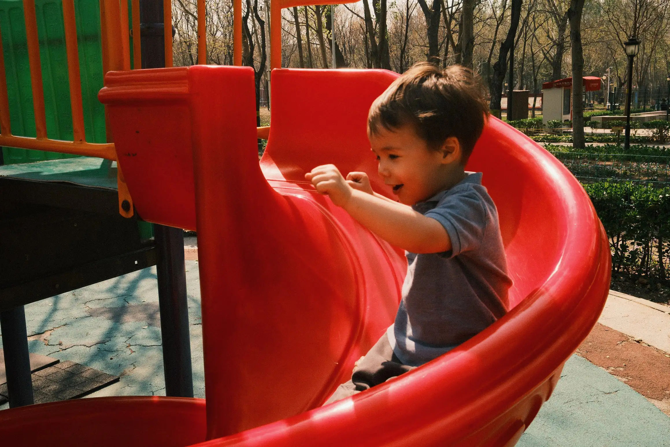 A boy smiles with delight as he slides down a small corkscrew slide. His arms up in the air to ensure he has maximum fun.