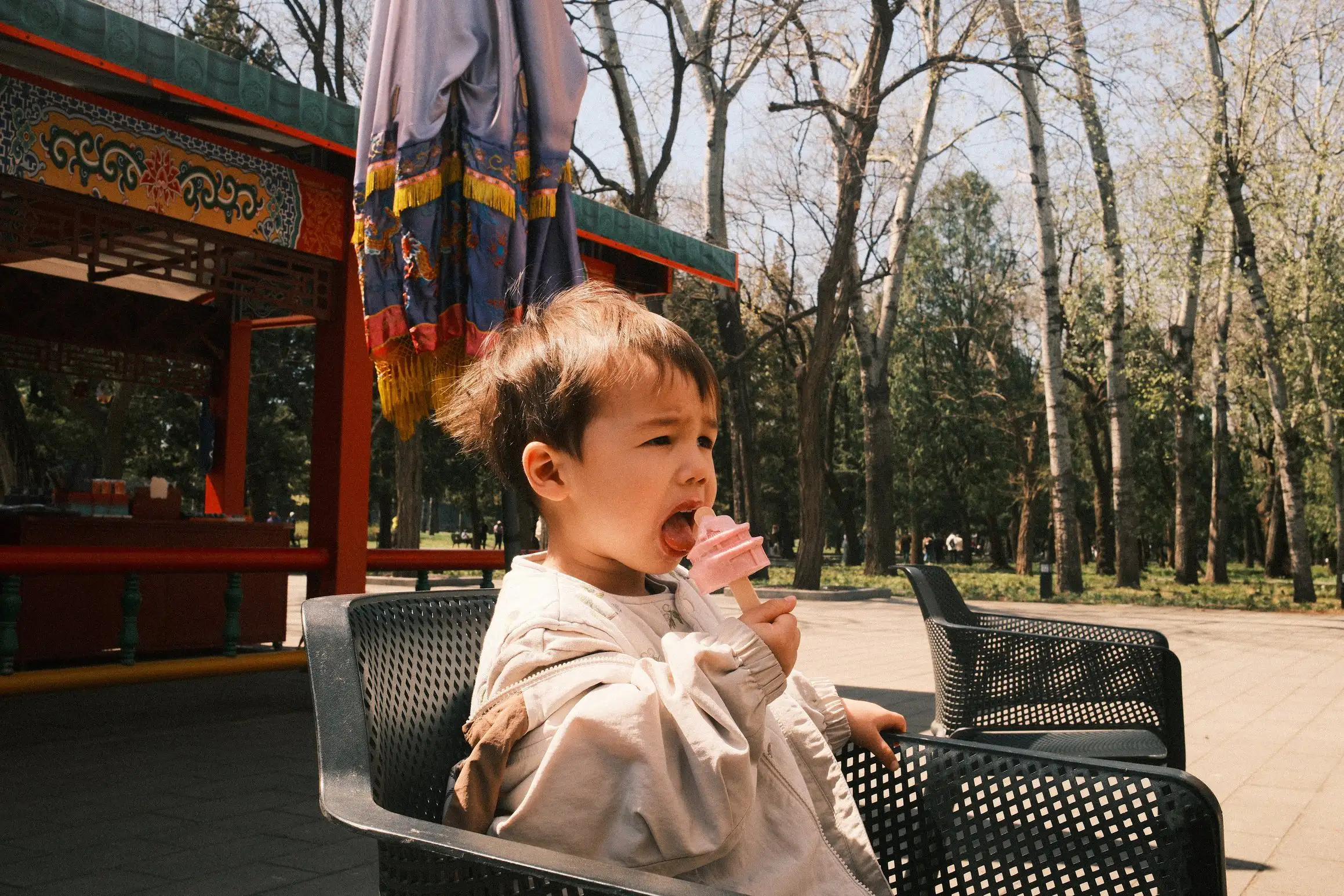 A boy sits on an outdoor chair eating an ice cream shaped like a temple.