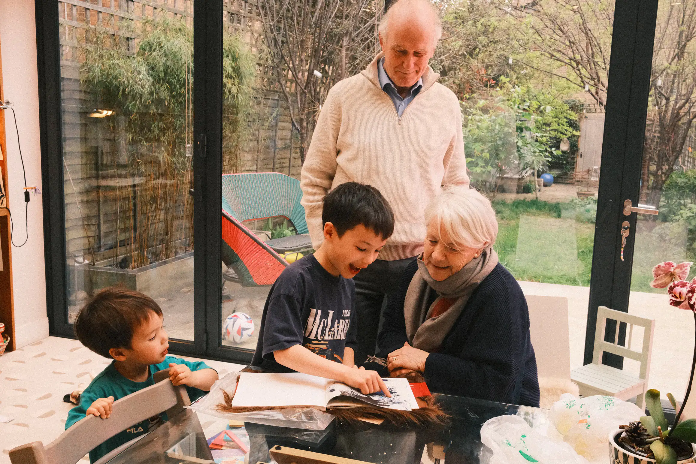 A family gathers round a table looking at something in a book.