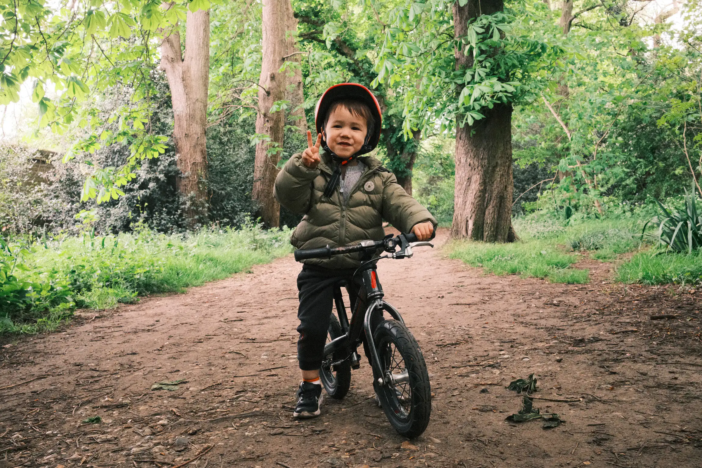 a young boy sits proudly on his balance bike on a dirt trail, trees in the background