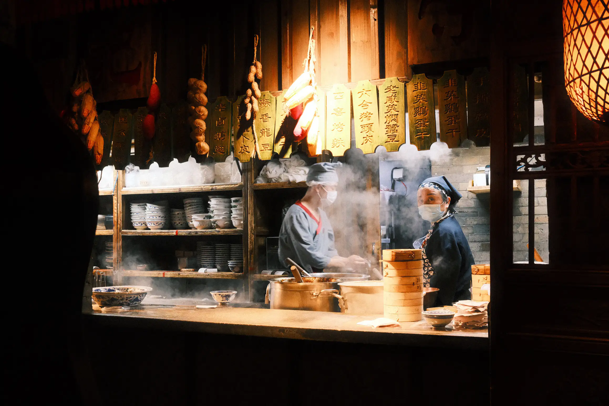 a chef looks towards the camera, steam rising from the stove in front of her