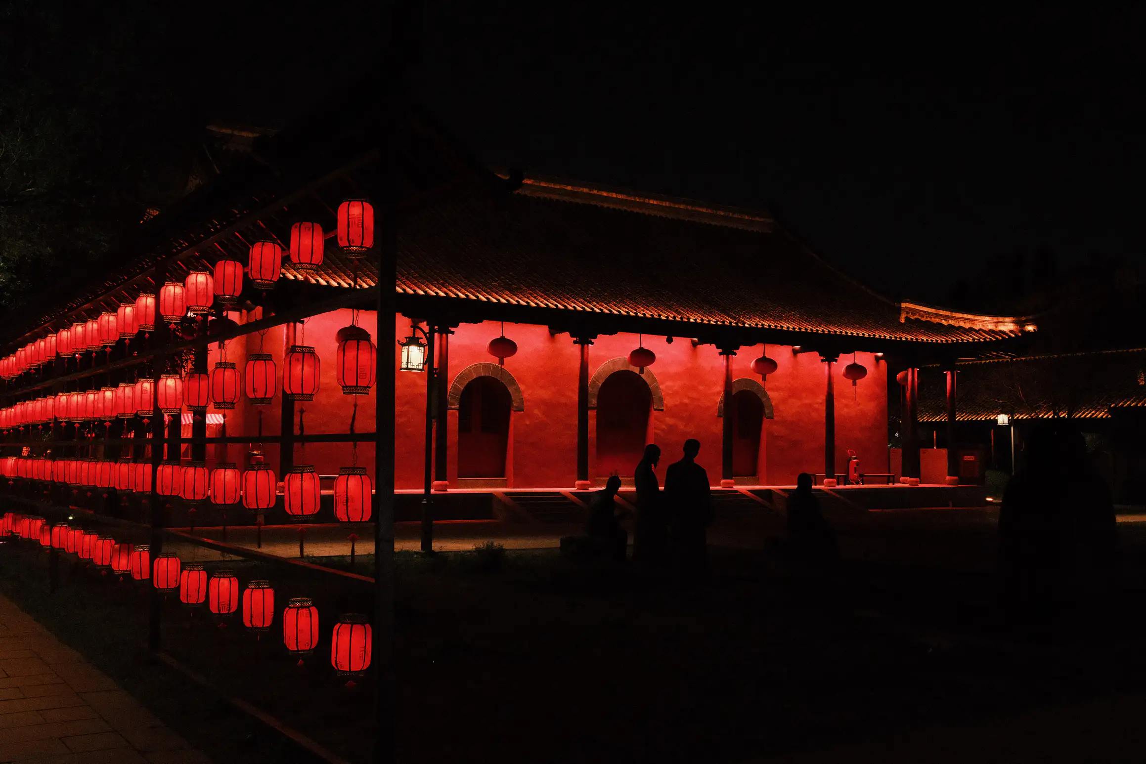a temple lit up at night, the red paint and red lanterns dominate the image