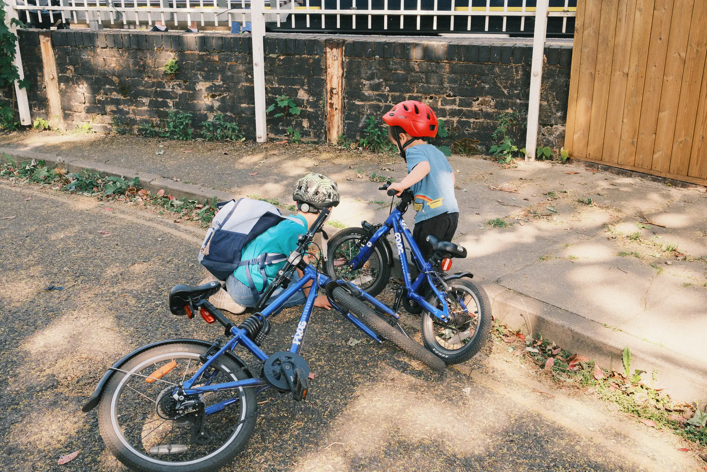 two boys stand by the side of the road, their bikes on the floor as they crouch looking at something by the kerb