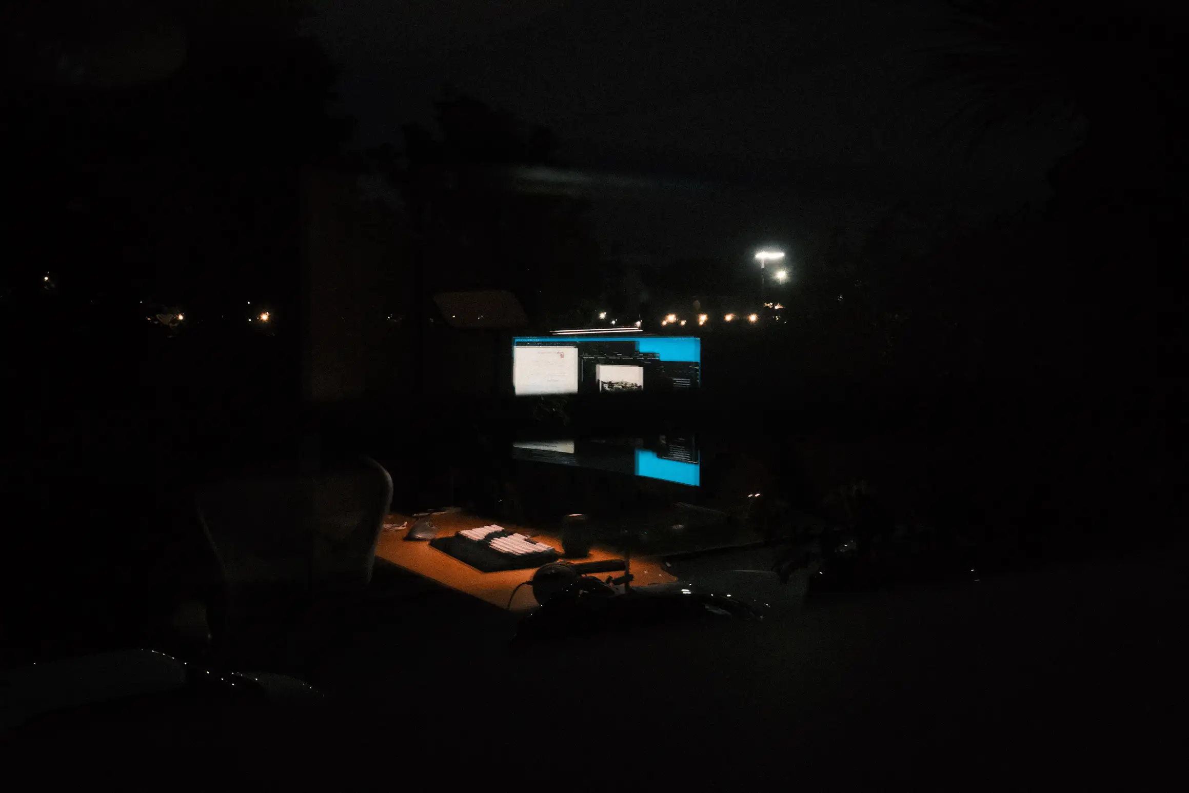 a photo of a night time reflection in an office window, the reflection shows a desk lit up by a computer monitor