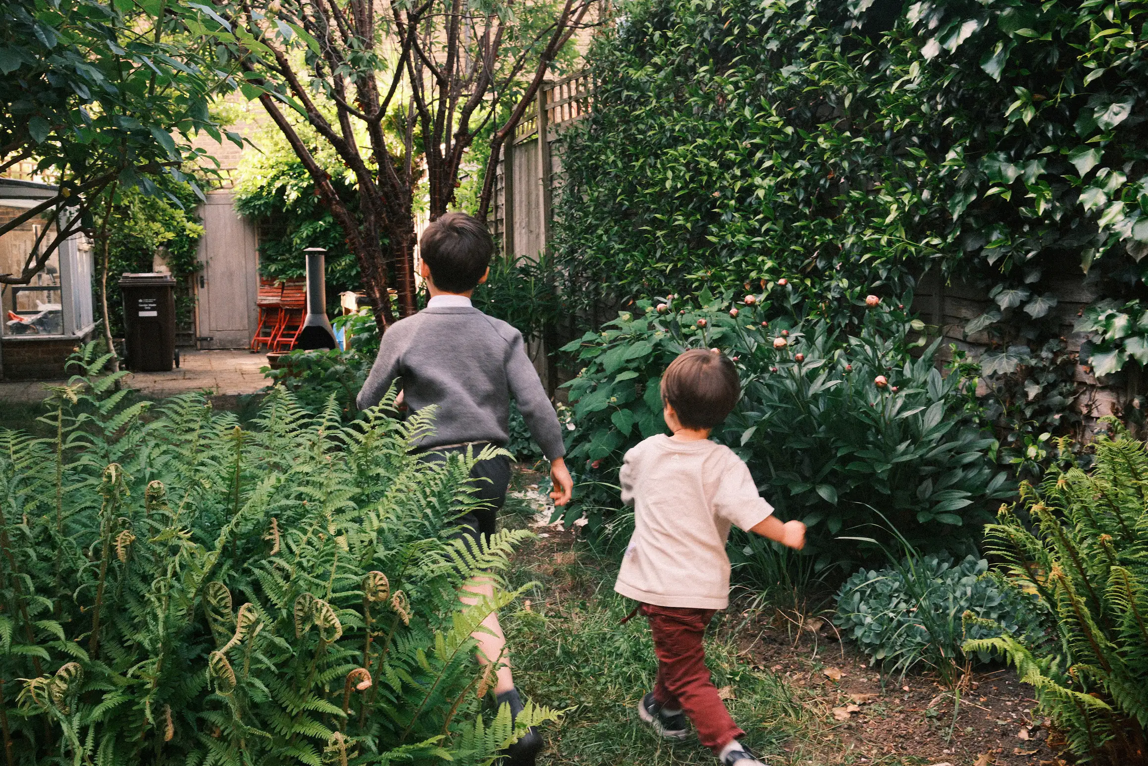 Two boys run out into a garden, the elder of them in school uniform.