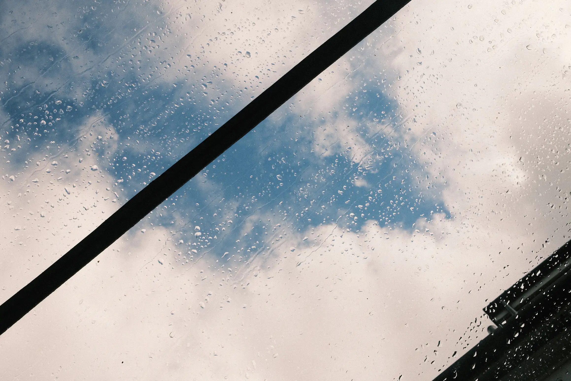 raindrops on a glass window, cloudy blue sky in the background