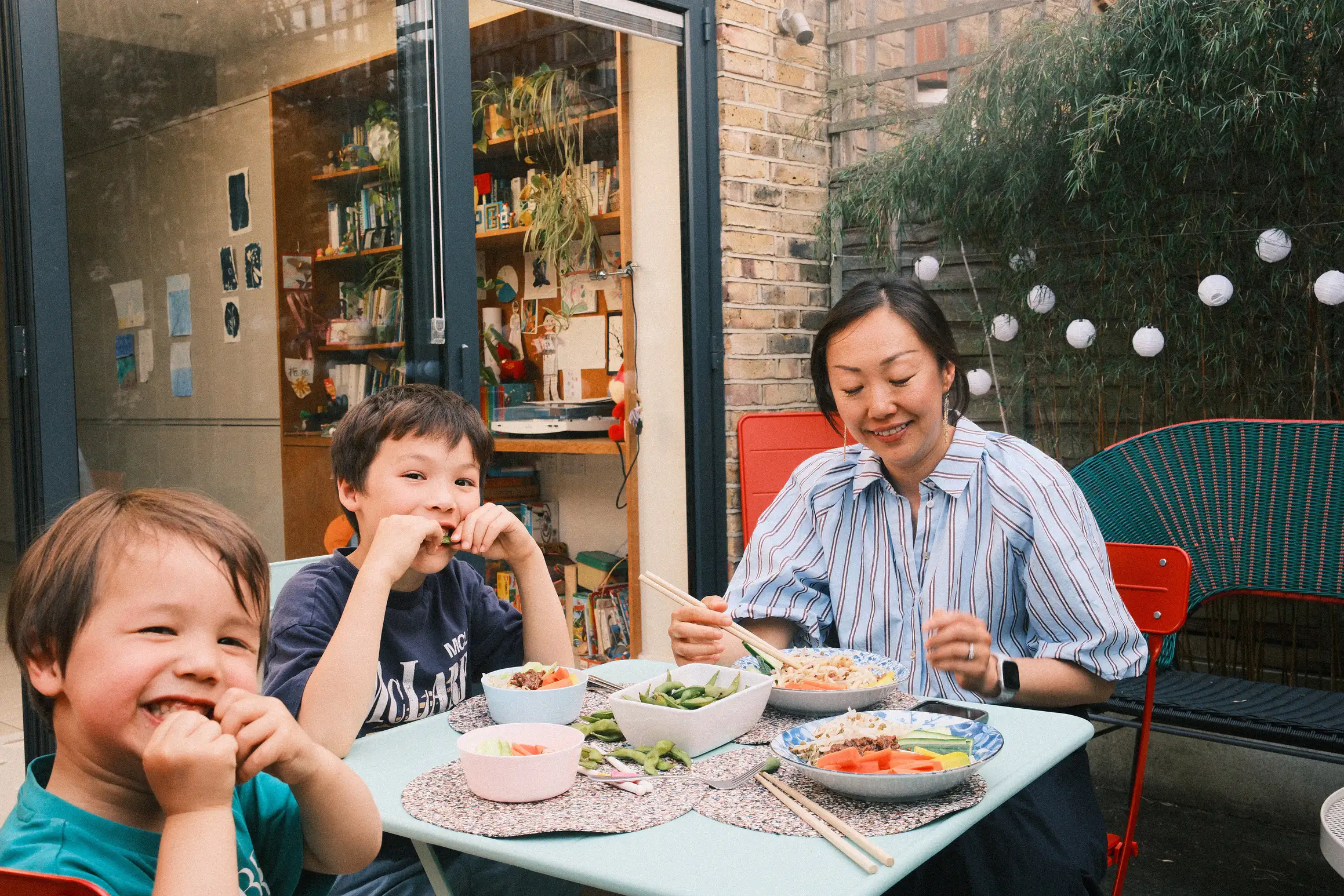 A family sit around a garden table eating, the two young boys turn to face the camera smiling