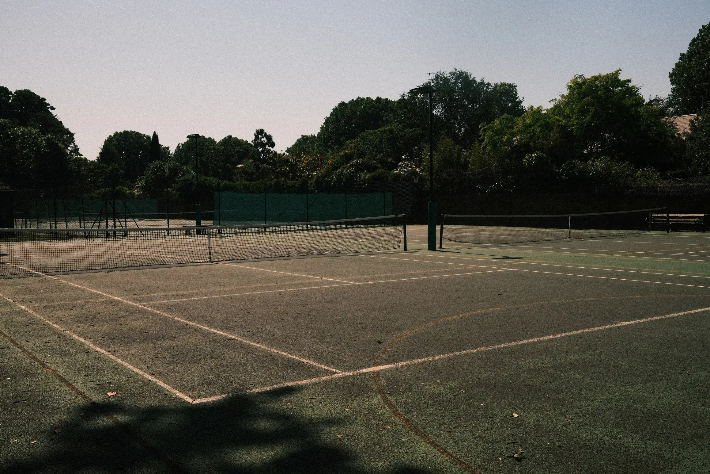An empty tennis court stands in the baking midday sun