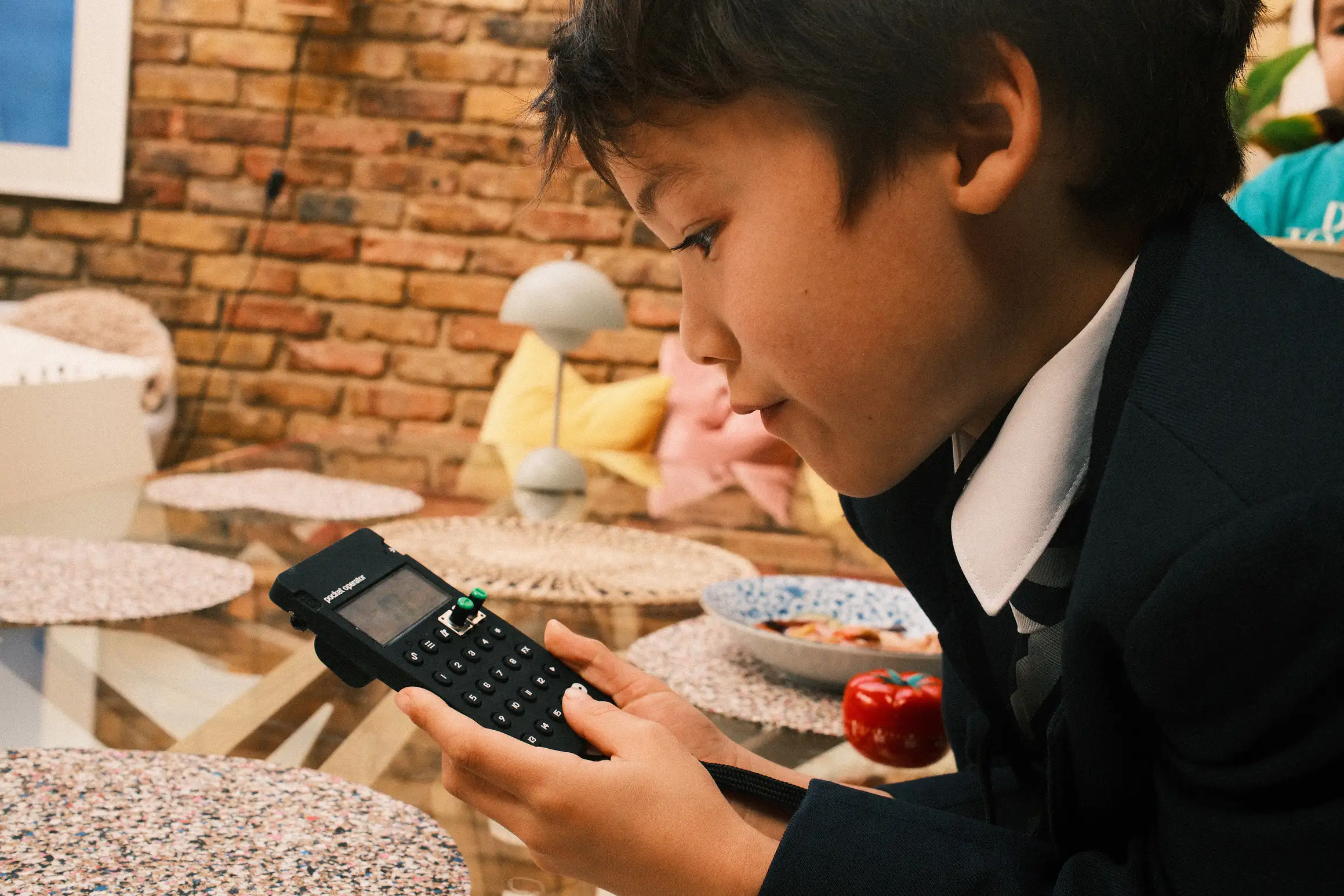 a photo of a boy playing with a Pocket Operator, a plate of food untouched behind him