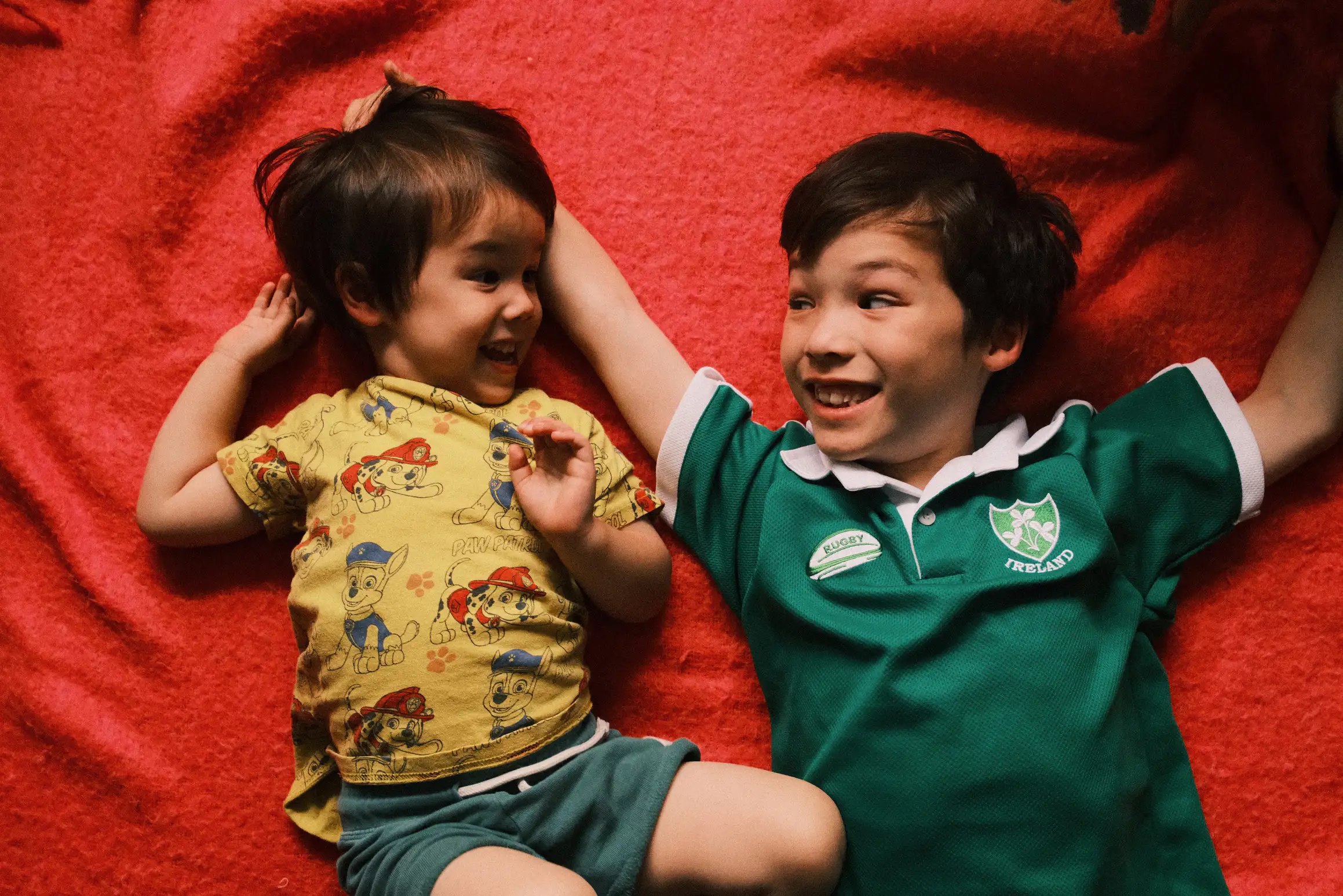 a photo of two boys laying on a rug smiling at each other