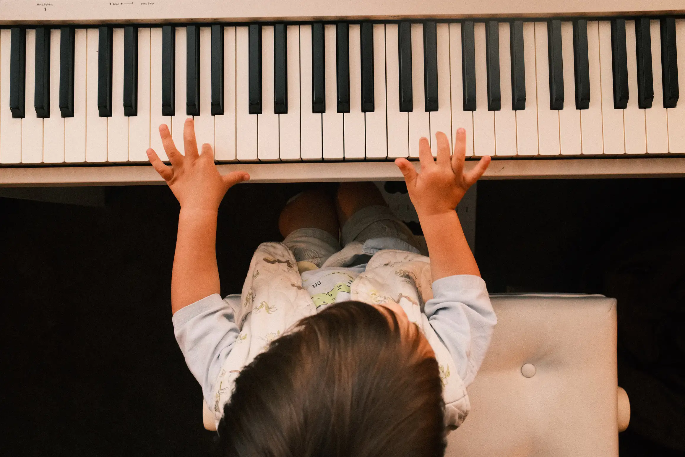 A photo looking down on a young child playing a piano.