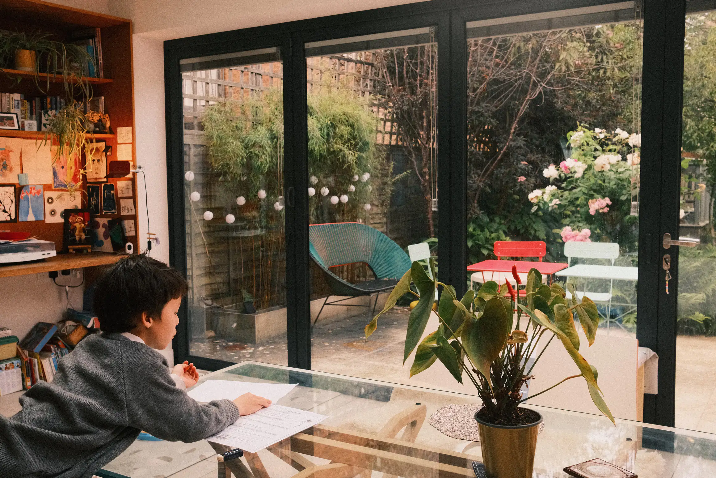 A photo of a young boy leaning over a glass table looking at two pieces of paper. 