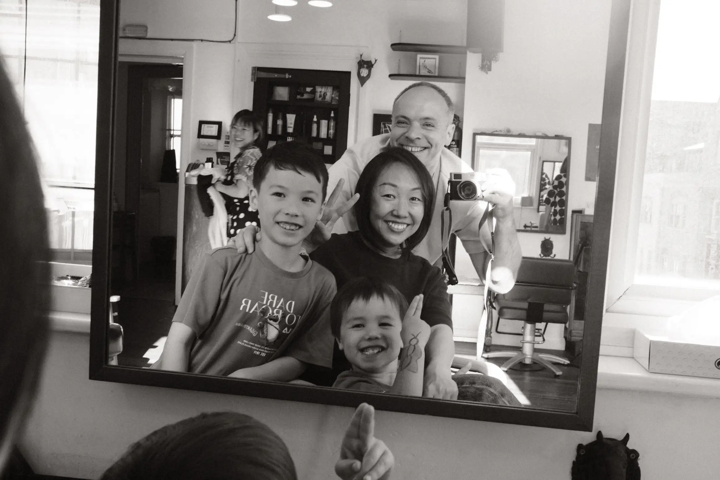 Black and white self-portrait of a family in the mirror at a barbershop.