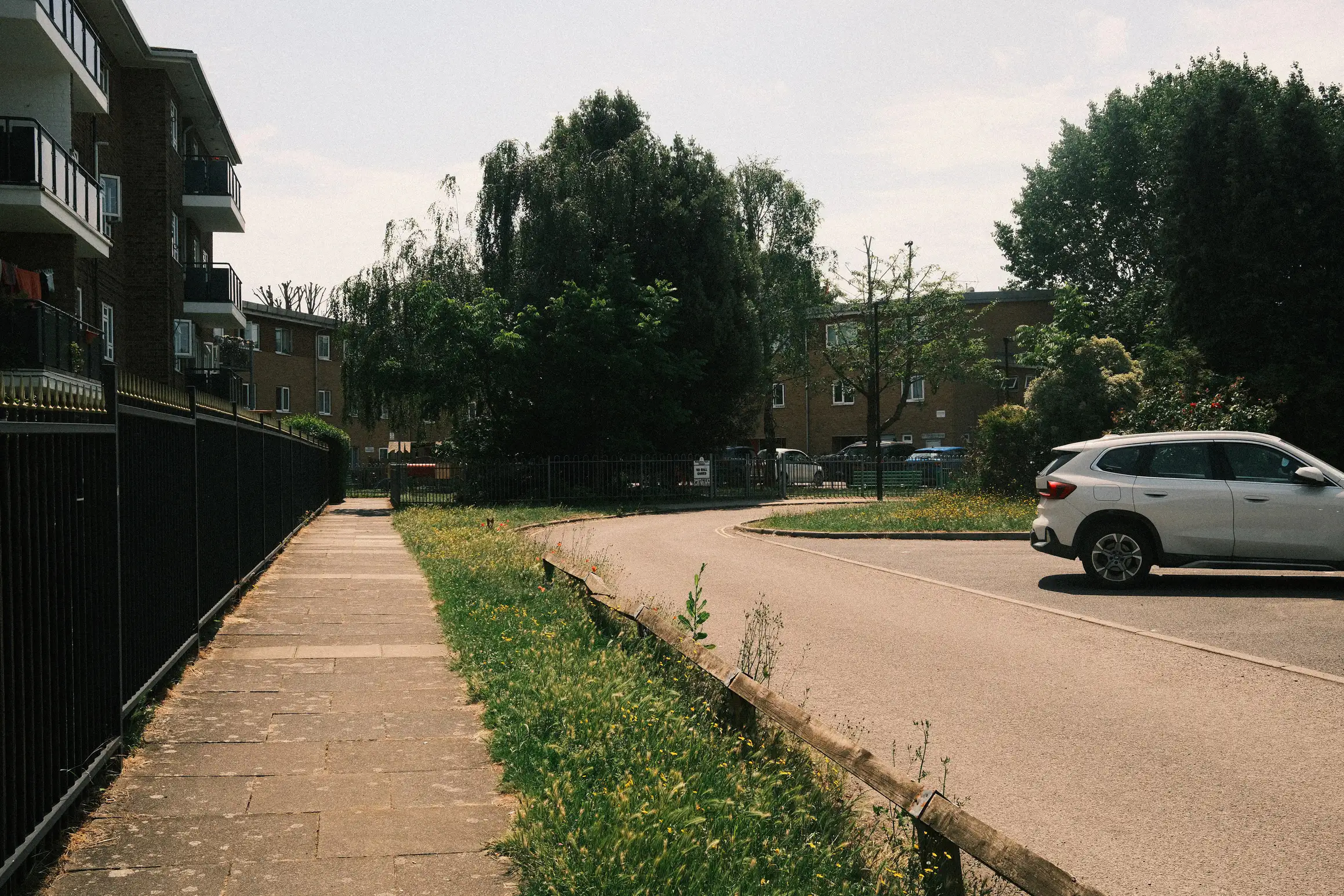 A photo of a deserted street. The pavement and road are lit by the midday sun. No people are out. 