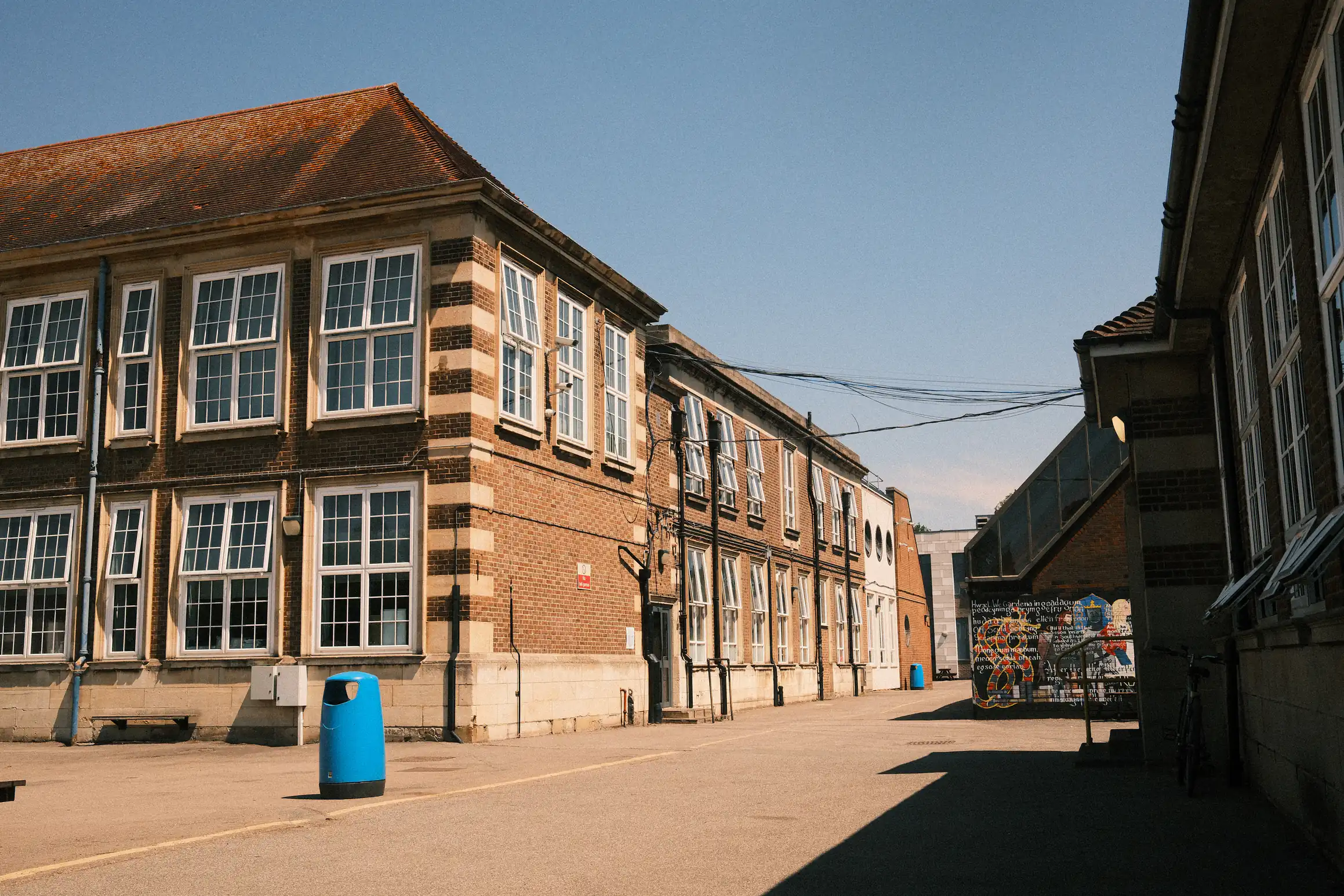 A photo of a school in the midday sun There are no people in the photo. To the right of the photo, a shadow is cast by the building nearest to the photographer.