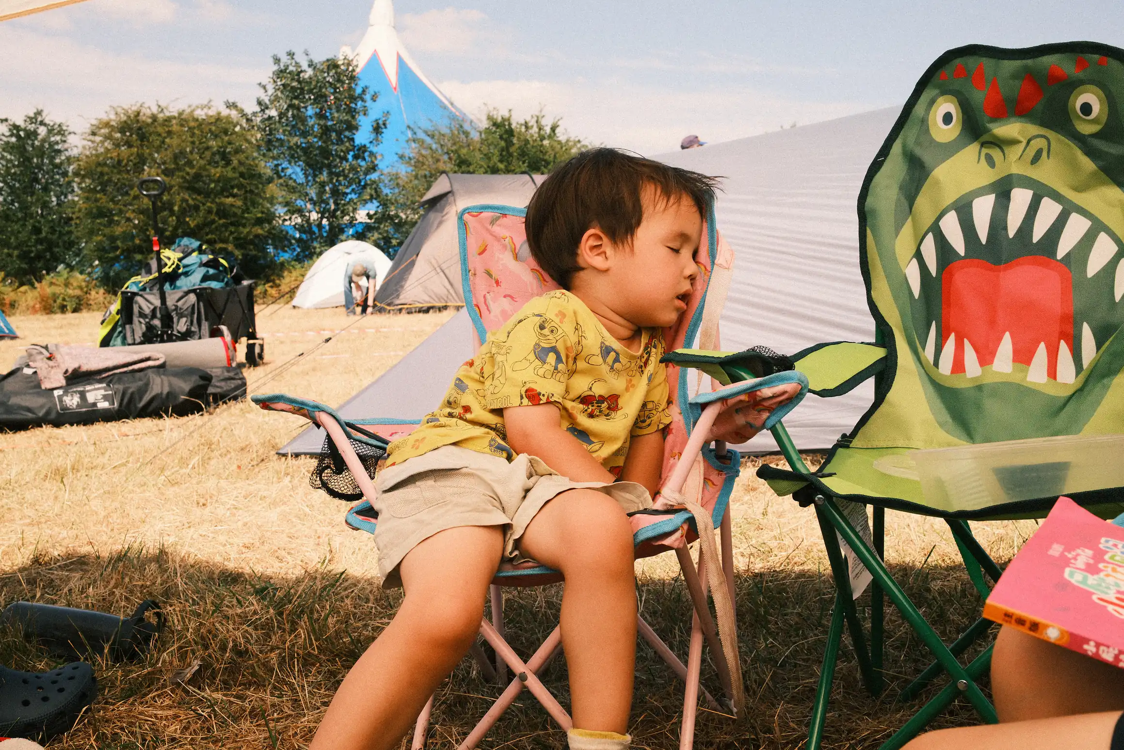 A tired boy sits in a camping chair behind him half-packed camping equipment, the end of an exhausting event 