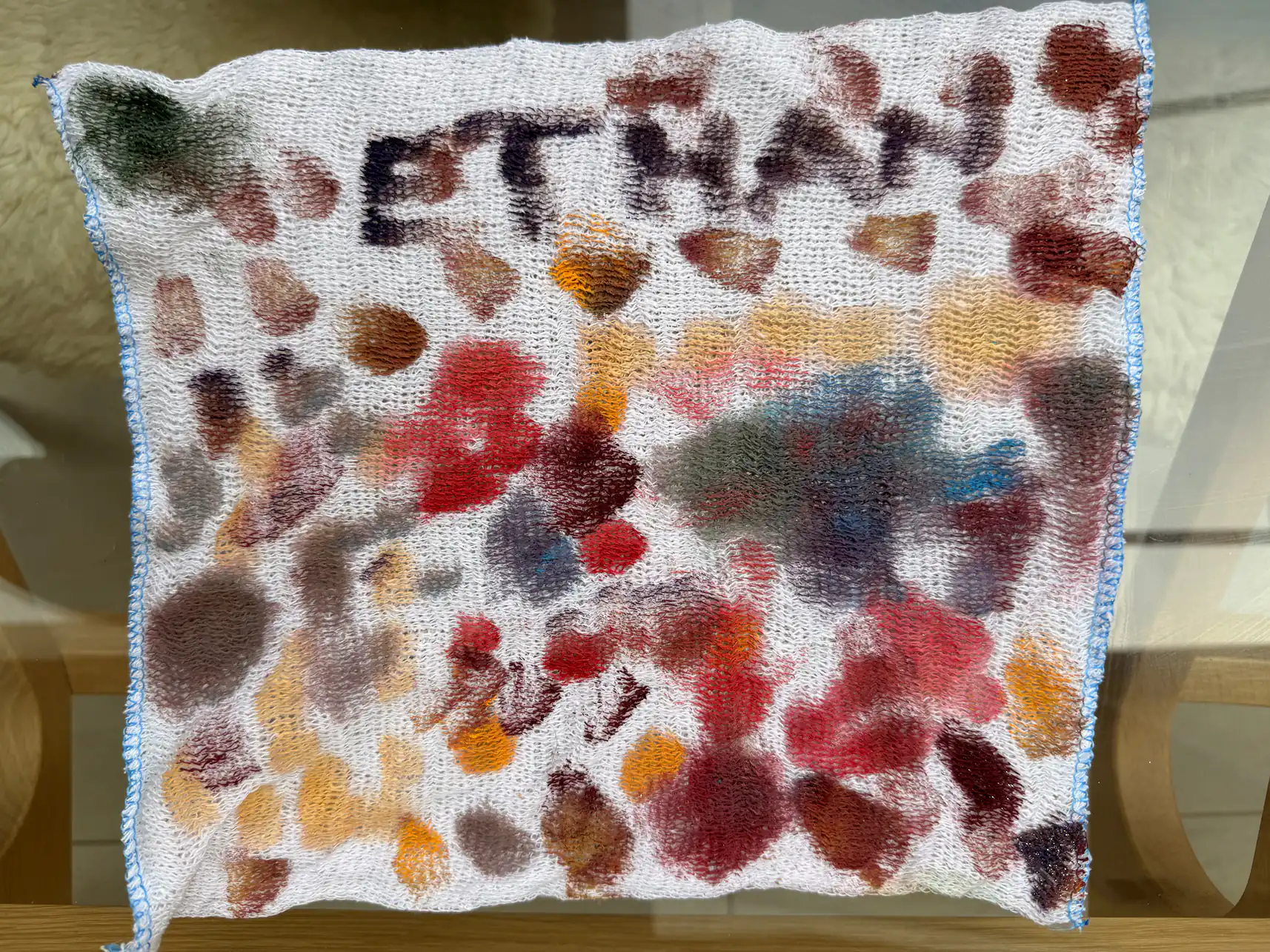 An otherwise clean dishcloth painted with colourful blobs of paint 