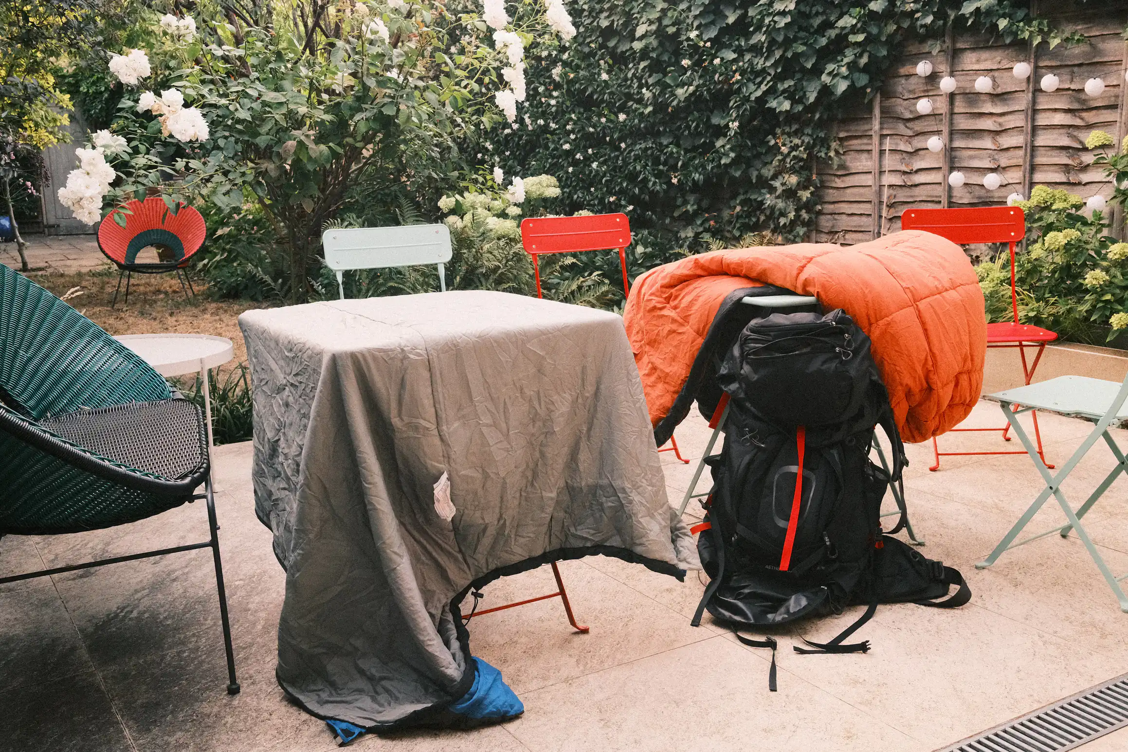 Two sleeping bags put out to air in a garden, they are draped over two square garden tables, in the background overly exposed greenery indicates it's a sunny day