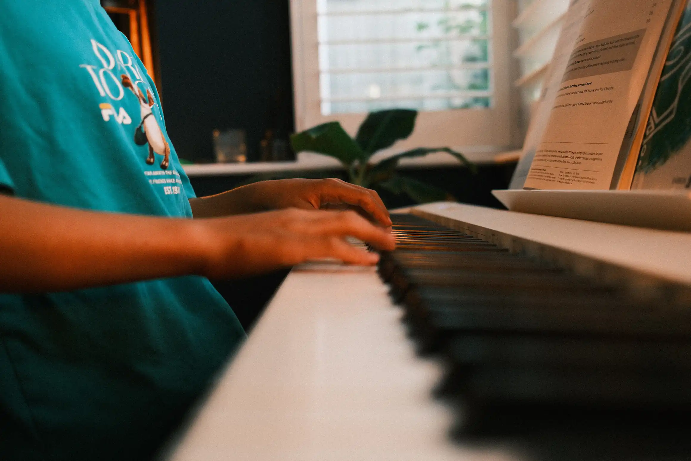 A photo looking along the length of a piano keyboard, the closest keys are blurred, with the focal point of the image being a pair of hands playing the keys