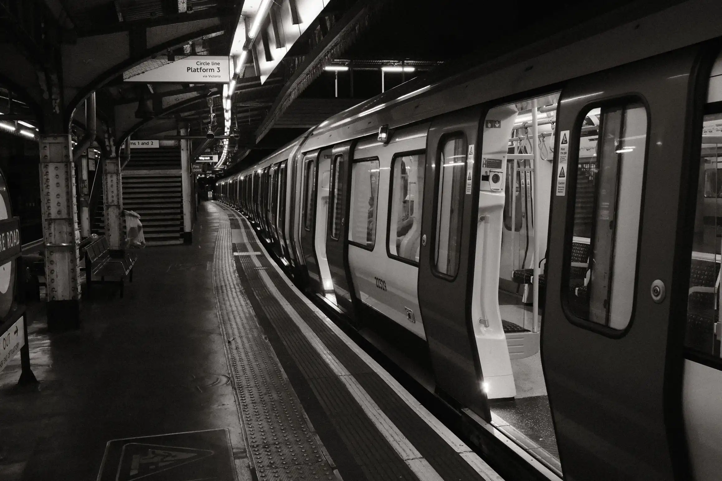 A black ad white photo taken on Edgeware Road station, the sign indicates this is platform 3, a train in the platform stands empty, it's doors open