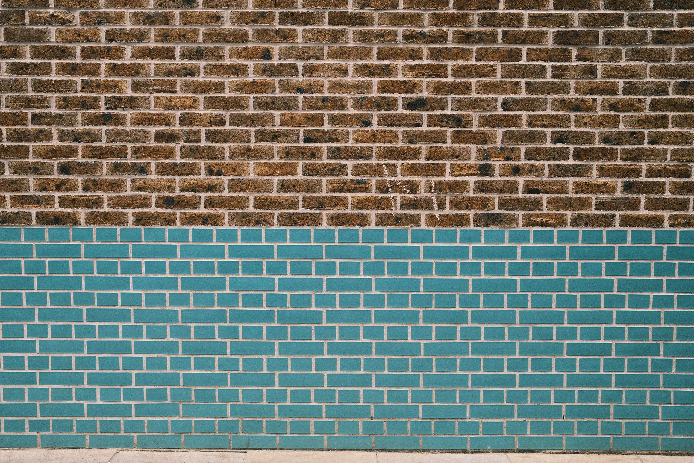 a photo of a brick wall, the top half of the wall is a traditional sandy brick colour, the bottom half is a deep turquoise