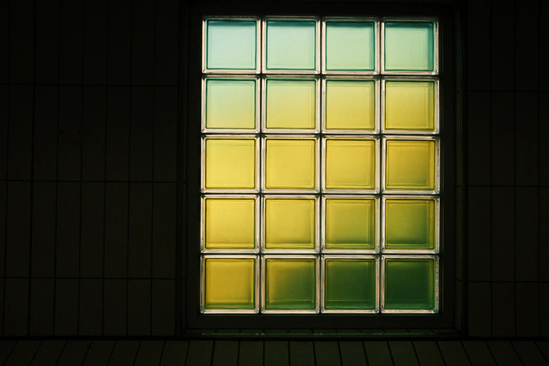 a photo of a window, the window is made up of 20 square panes, 4 across and 5 hight, the colour of the glass fades diagonally from turquoise top left, through yellow, to green in the bottom right