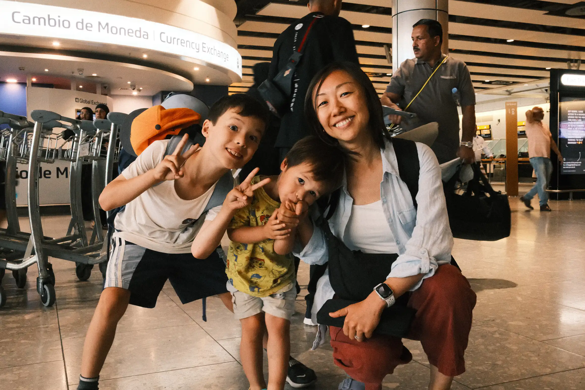 A family kneels on the ground in the departure lounge of Heathrow Airport, bags packed, checked in, ready to fly. The youngest seems unsure.