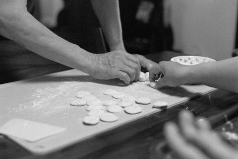 A black and white photo showing two people making dumpling skins. Only their arms and hands are visible, we don't get to see their faces. The image is a scan of a negative developed at home in Ilfosol3 (1+9).