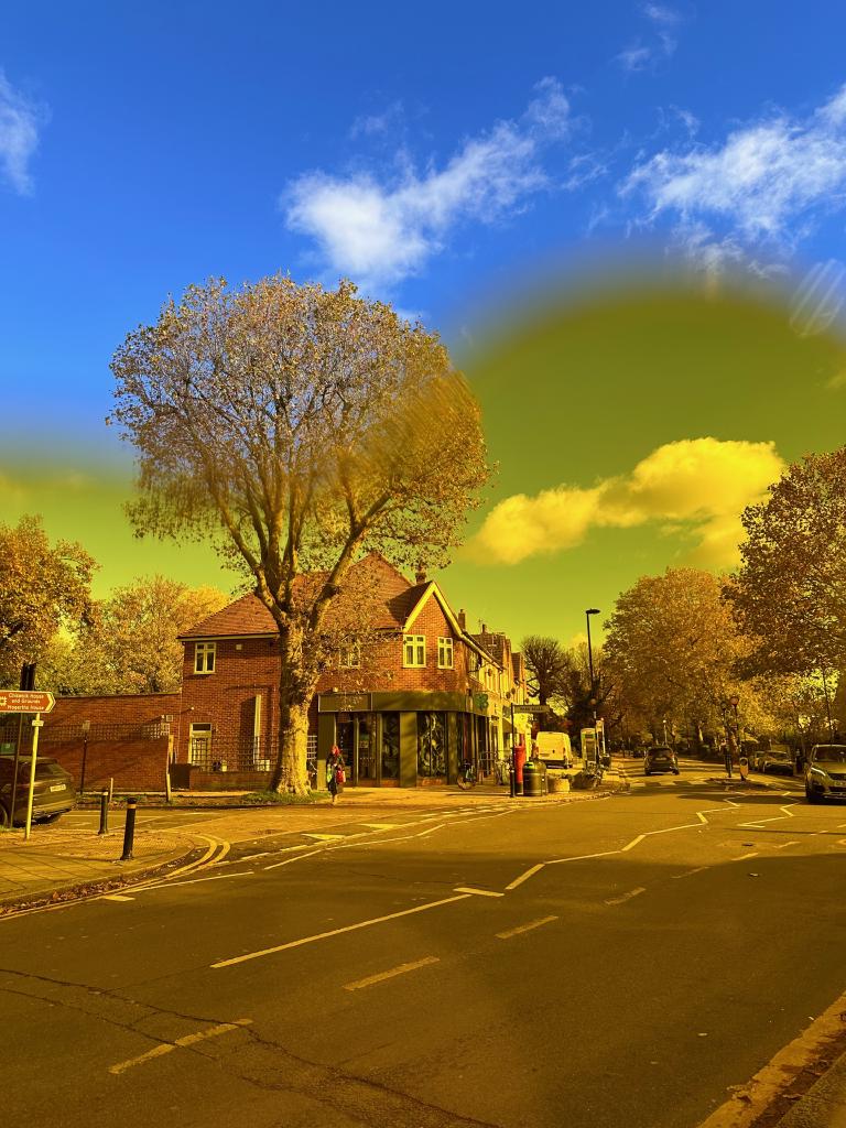 This is an image of two halves. The scene is a street corner in West London, the top half of the image is unfiltered, a bright blue sky with the occasional fluffy white cloud. The lower half of the image is shot through yellow tinted glasses. The sky is almost green, a strong yellow tint giving a sense of warmth.