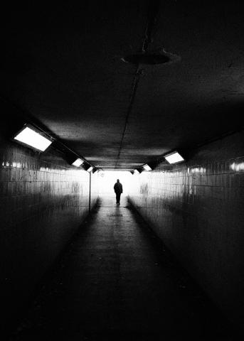 A black and white photo of a person at the far end of the subway. Their figure is silhouetted against the bright light streaming in from the entrance. Which way will they turn: left or right?